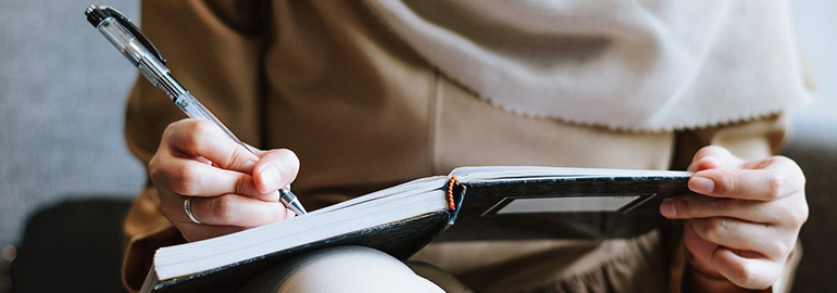 Woman sitting on a couch writing in a notebook