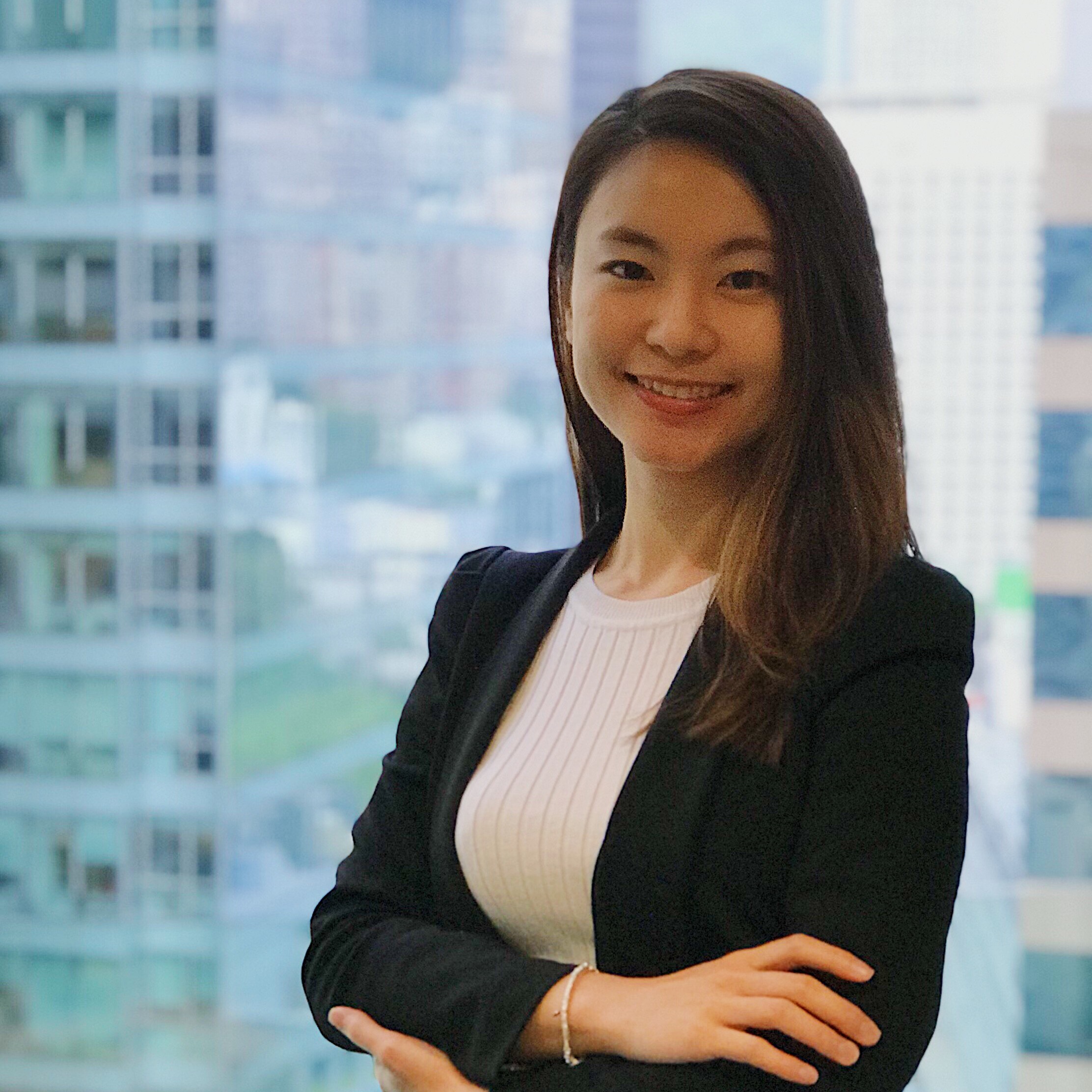 Young woman in a black blazer smiling in front of a cityscape.