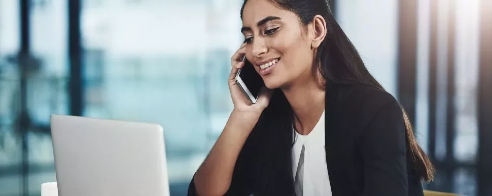 Smiling woman on a phone call while working on a laptop.