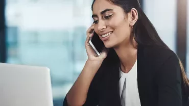 Smiling woman on a phone call while working on a laptop.