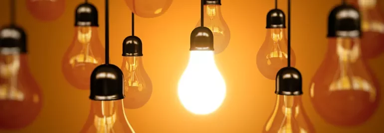 A group of hanging lightbulbs with one brightly lit.