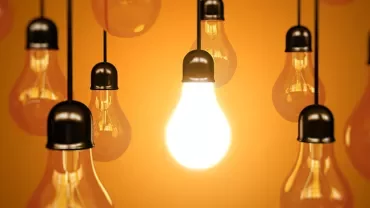 A group of hanging lightbulbs with one brightly lit.