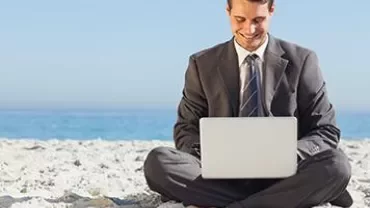 Smiling man in a suit working on a laptop at the beach.