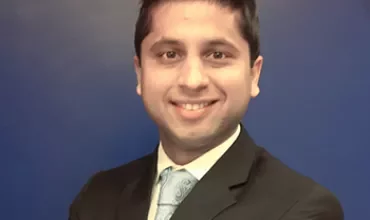 Man in a suit smiling with a blue background.