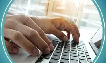 Person typing on a laptop keyboard with bright sunlight through a window.