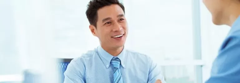 Smiling man in a blue shirt talking with a colleague in an office.