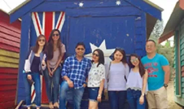 Group of people posing in front of a blue beach hut with an Australian flag design.