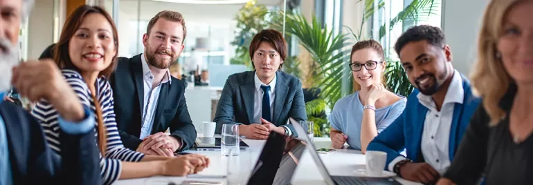 Team of diverse professionals in a meeting room with laptops.