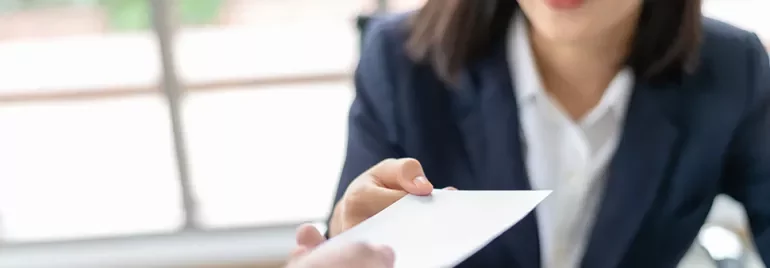 Close-up of a person in a suit handing over an envelope.