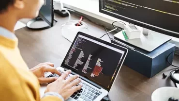 Person typing code on a laptop with a larger screen showing more code.