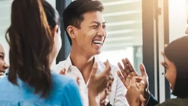 Group of colleagues smiling and clapping in a meeting.
