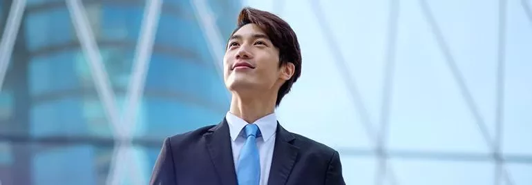 Confident man in a suit looking up, blue building background.