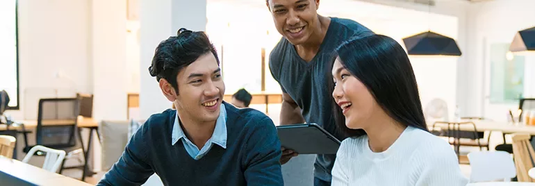 Three colleagues laughing and working together in a modern office.