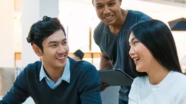 Three colleagues laughing and working together in a modern office.