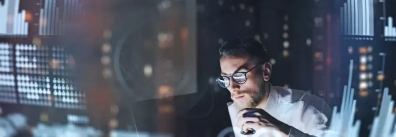 Man in glasses analyzes data on computer with blurred charts.