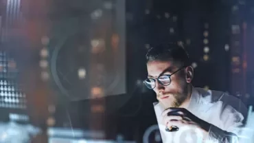 Man in glasses analyzes data on computer with blurred charts.