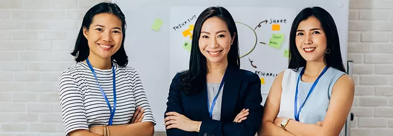 Three women smiling, standing in front of a whiteboard with sticky notes.