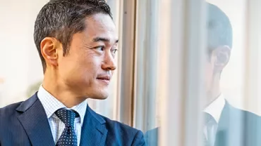 Man in a suit looking out the window with reflection visible.