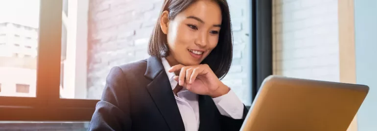 Businesswoman smiling while working on a laptop at her desk.