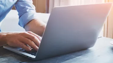 Person typing on a laptop at a wooden table with a cup of coffee nearby.