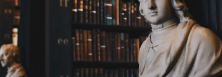 Marble bust in a historic library with bookshelves in the background.