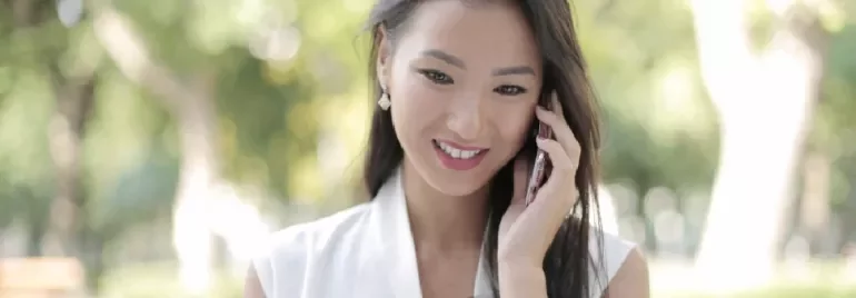 Woman smiling while talking on a smartphone outdoors.