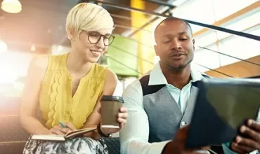 Two people collaborating in an office with a tablet and coffee.