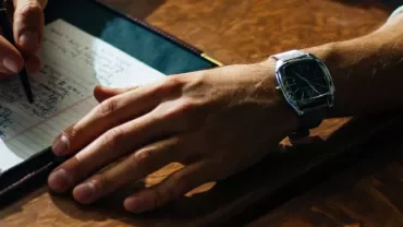 Person writing notes with a black pen at a wooden desk.