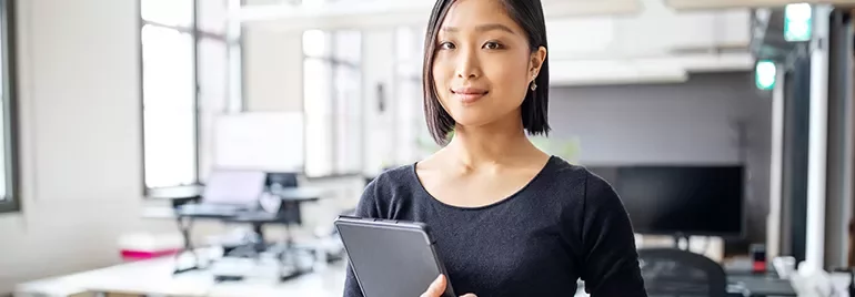 Woman in office holding tablet with large windows.