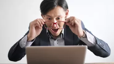 Man with glasses looking surprised at laptop screen.