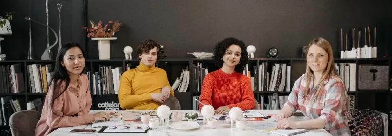 Four people sitting at a table in an office setting, with bookshelves in the background.
