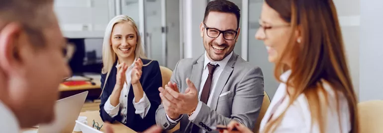 A group of business professionals sitting at a table, laughing and clapping during a meeting.