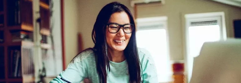 Smiling person with glasses working at a laptop in a cozy room.