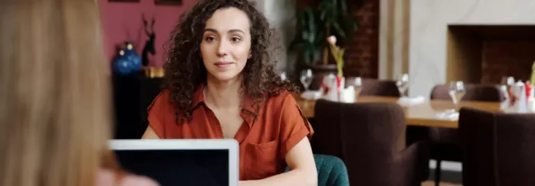 Woman with curly hair in red blouse talking at a cafe.