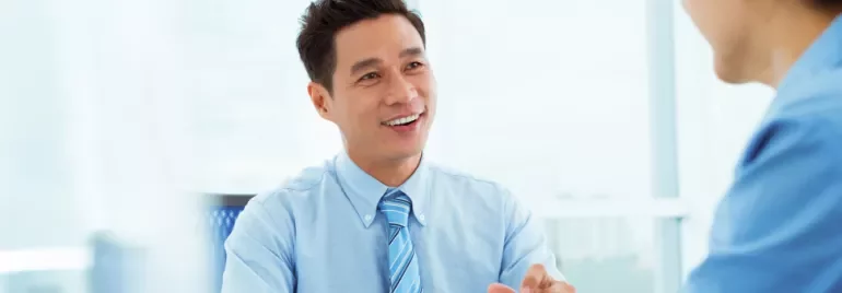 Man in blue shirt smiling at a colleague during a meeting.