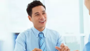 Man in blue shirt smiling at a colleague during a meeting.