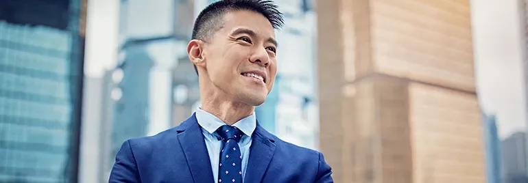 Smiling man in a blue suit stands confidently with city skyscrapers in the background.