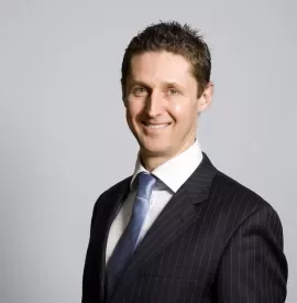 Smiling man in a suit and tie with a neutral background.