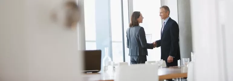 A man and woman shaking hands in a conference room, indicating a formal agreement or partnership.