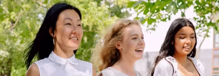Three women walking outdoors, smiling and enjoying a sunny day.
