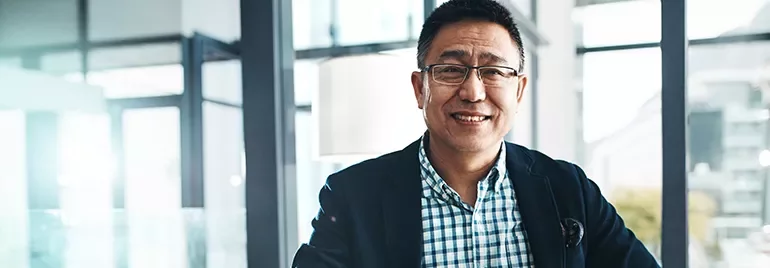 Smiling person in a checked shirt and blazer, in a bright modern office.