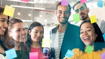 A group of diverse colleagues brainstorming with colorful sticky notes on a glass wall.
