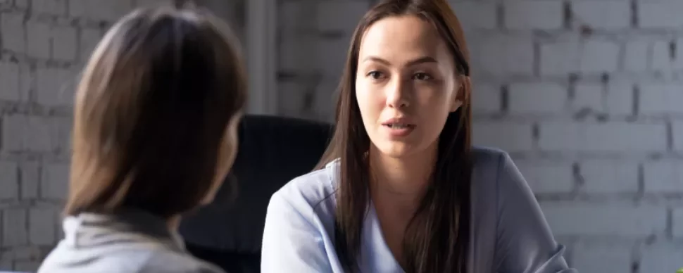 Two women engaged in a serious conversation inside an office.