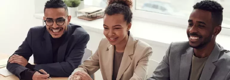 Three people sitting at a table in a meeting, smiling.