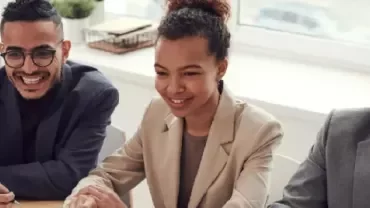 Three people sitting at a table in a meeting, smiling.