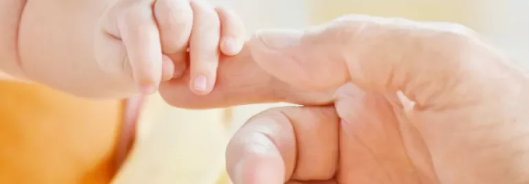 A baby's hand holding an adult's finger gently.