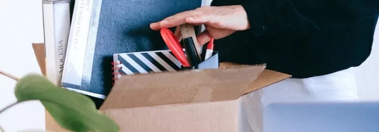 Person organizing stationery and books in a cardboard box.