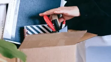 Person organizing stationery and books in a cardboard box.