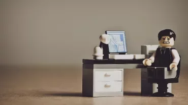 Lego figure at a desk with a computer, looking distressed.