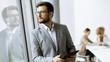 Businessman in a suit with a tablet, looking out of a window.